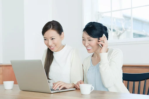 Mother using mobile phone next to daughter using laptop