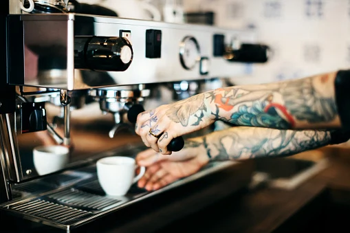 Tattooed hands preparing cup of coffee.