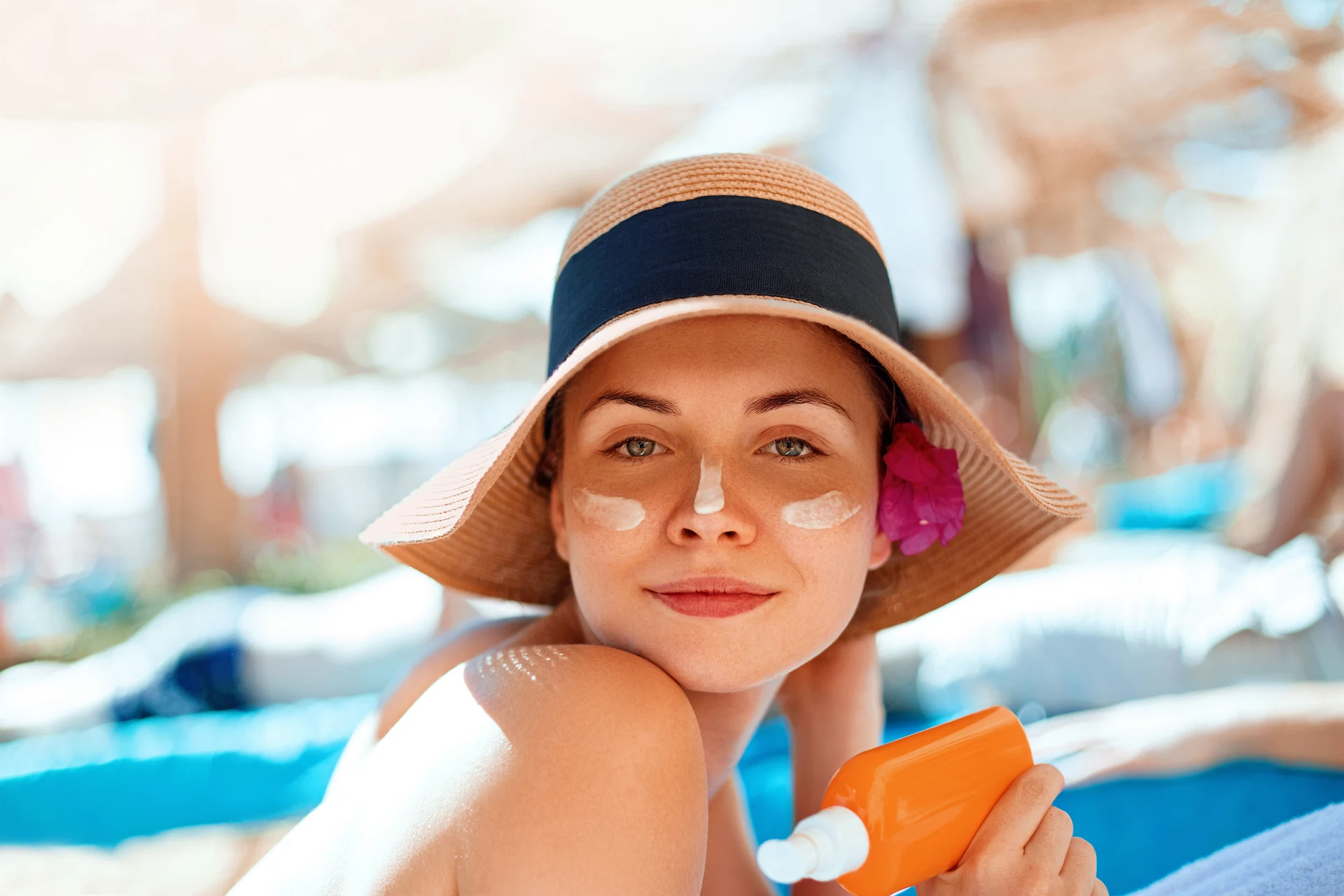 Young woman with sun cream on face holding sunscren bottle on the beach. Female in hat applying moisturizing lotion on skin. Young woman with sun cream on face holding sunscren bottle on the beach. Female in hat applying moisturizing lotion on skin.